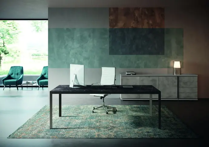 Scopri la linea direzionale D1 – Essenzialità e prestigio per ambienti manageriali moderni Scrivania direzionale con piano effetto marmo nero, sedia bianca e madia grigia in ambiente elegante con tappeto e poltrone verdi vicino alla vetrata